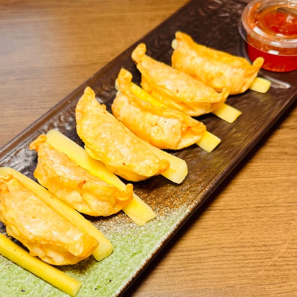 Hana Hawaiian BBQ's golden-fried dumplings and vegetable sticks on a dark plate with dipping sauce.