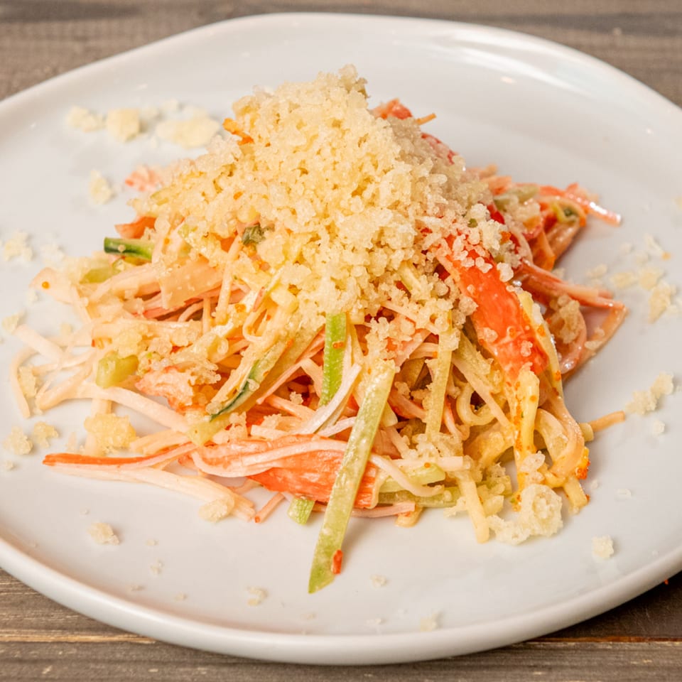 Hana Hawaiian BBQ's crab salad with shredded crab, cucumber, and crispy tempura flakes on a white plate.