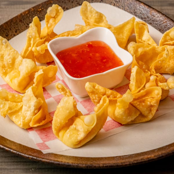 Crispy golden wontons arranged on a plate with a heart-shaped bowl of sweet chili dipping sauce.