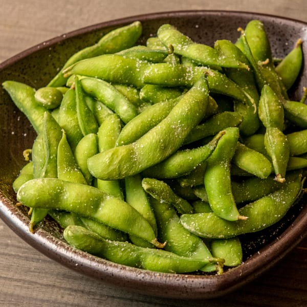 A dark bowl filled with vibrant green edamame pods, lightly sprinkled with sea salt.